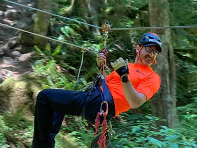 A rescuer in an orange shirt and helmet suspends from a rope with a smile on their face