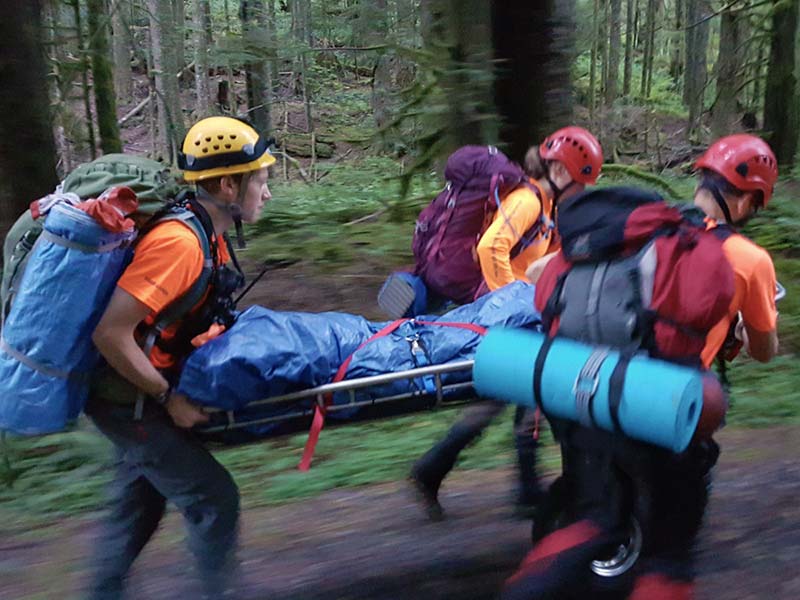 Search and rescue members wearing orange evacuating a person in a sked on a trail in the forest during a training